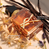 A rectangular YSL Libre Intense 3.0 oz. EDP Women Perfume bottle rests among orange blossoms, vanilla beans, and lavender sprigs, with labels for Vanilla Bourbon, Orange Blossom, and Diva Lavender.