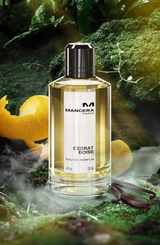 A bottle of Mancera Intense Cedrat Boise 4.0 oz. EDP Women Perfume with a yellow liquid, standing in a mossy, forest-themed setting with citrus peels nearby.