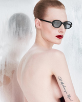 A person with slicked-back hair, bold red lipstick, and Tom Ford Sunglasses FT1364/S 52N poses with their back to the camera. A script tattoo is visible on their arm, reflected in the foggy glass behind them.