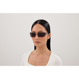 A woman with long, straight black hair in a white top wears Balenciaga Sunglasses BB0485SA-001 76, standing against a plain light background and looking directly at the camera with a neutral expression.