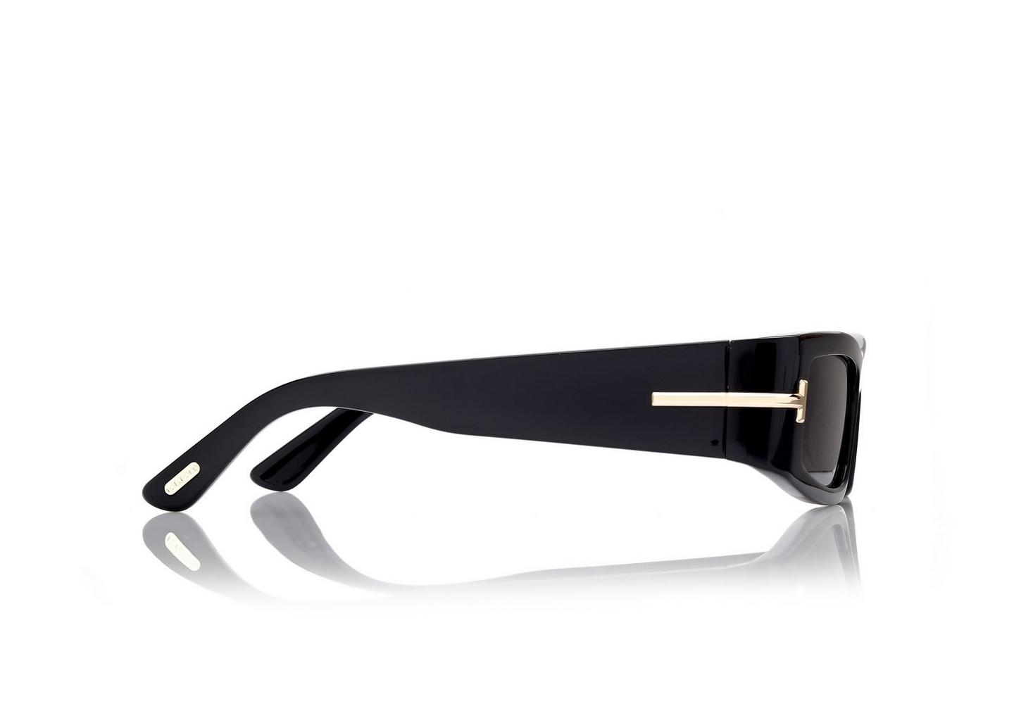Tom Ford ICON TI0026/S 01Z sunglasses, shown side-on, feature a black rectangular frame with thick arms and subtle gold detailing near the hinge—designer eyewear by Tom Ford Sunglasses on a white background with a faint reflection.