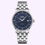 The Mido Watches Baroncelli Signature Gent M0374071104100, featuring a silver case, blue dial with thin hour markers, date display at 3 o’clock, and a metal link bracelet—powered by the precise MIDO Caliber 80 Swiss automatic movement—is displayed against a light lavender background.