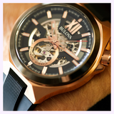 Bulova 98A177 Maquina Automatic Black Silicone Strap men’s watch in rose gold-tone with an exposed mechanical movement and black dial.