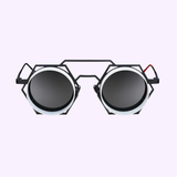 Vysen Sunglasses’ Vysen Nikky - NK4 Unisex Sunglasses feature a handcrafted geometric hexagonal black frame with round dark lenses and sleek silver rims, made in Italy. Displayed on a light purple background, these luxurious sunglasses are accented by a small red detail on the right temple.