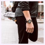 A person wearing a Bulova 98A177 Maquina Automatic Black Silicone Strap Men Watches with a gold-tone case and skeleton dial while stretching on a city street.