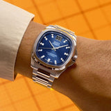 A Mido Watches Multifort TV Big Date Chronometer M0495671104100 featuring a square-cased silver wristwatch with a blue patterned dial, a large date display at the 12 o’clock position, and a stainless steel link bracelet.