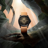 The Mido Watches Multifort TV Big Date M0495263608100, a Swiss automatic timepiece from Mido Watches featuring a tan leather strap, is showcased on a gnarled tree branch among lush green leaves and sunbeams streaming through a misty, forest-inspired setting. Driven by the precise Caliber 80 movement, this watch exemplifies the harmonious fusion of elegance and innovation amid the serene beauty of nature.