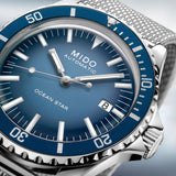 Close-up of a Mido M0268071104101 OCEAN STAR TRIBUTE automatic diving watch by Mido Watches in blue, displaying the time as 10:09 with a date indicator and a textured metal strap.