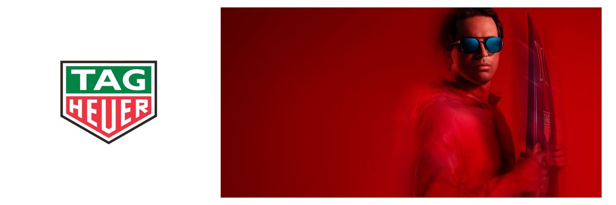 A TAG Heuer logo appears on the left, while a man in sunglasses and a red outfit stands on the right, holding a surfboard against a solid red background.
