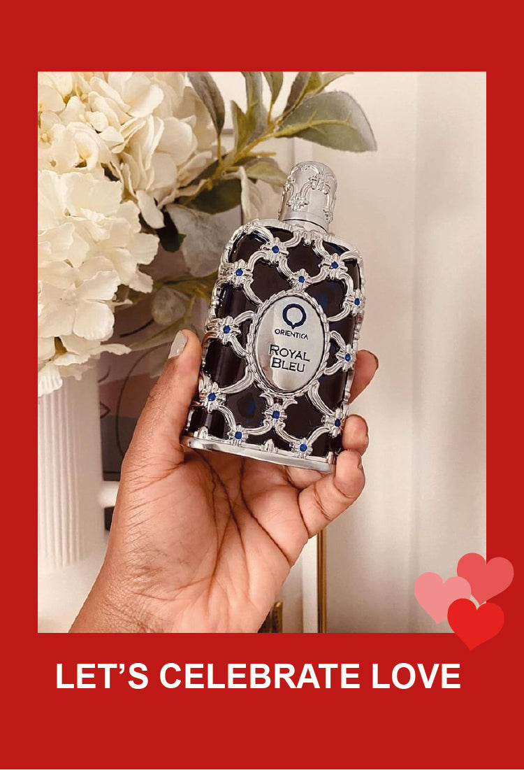 A hand holds an ornate bottle of Orentica Royal Bleu perfume in front of white flowers. The image has a red border with heart graphics and the text LET’S CELEBRATE LOVE at the bottom.