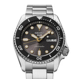 The Seiko Watches 5 Sports SKX series SRPL79 is an automatic watch featuring a stainless steel band, a black bezel, and a black dial with gold accents. It includes luminous markers and hands, as well as a day and date display at the 3 o’clock position.