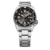 A Seiko Watches 5 Sports SKX series SRPL79 automatic wristwatch featuring a silver metal band, black bezel, gray dial with yellow hour markers, and a day-date display indicating MON 6.