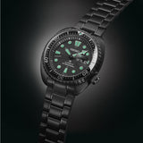 Introducing the Seiko Watches The Black Series Prospex Sea SRPK43 by Seiko Luxe Watches: an automatic dive watch with a black case and metal bracelet, featuring green-glowing luminescent hour markers and hands that exemplify Japanese watchmaking expertise. The day and date display is conveniently located on the right side of the dial.