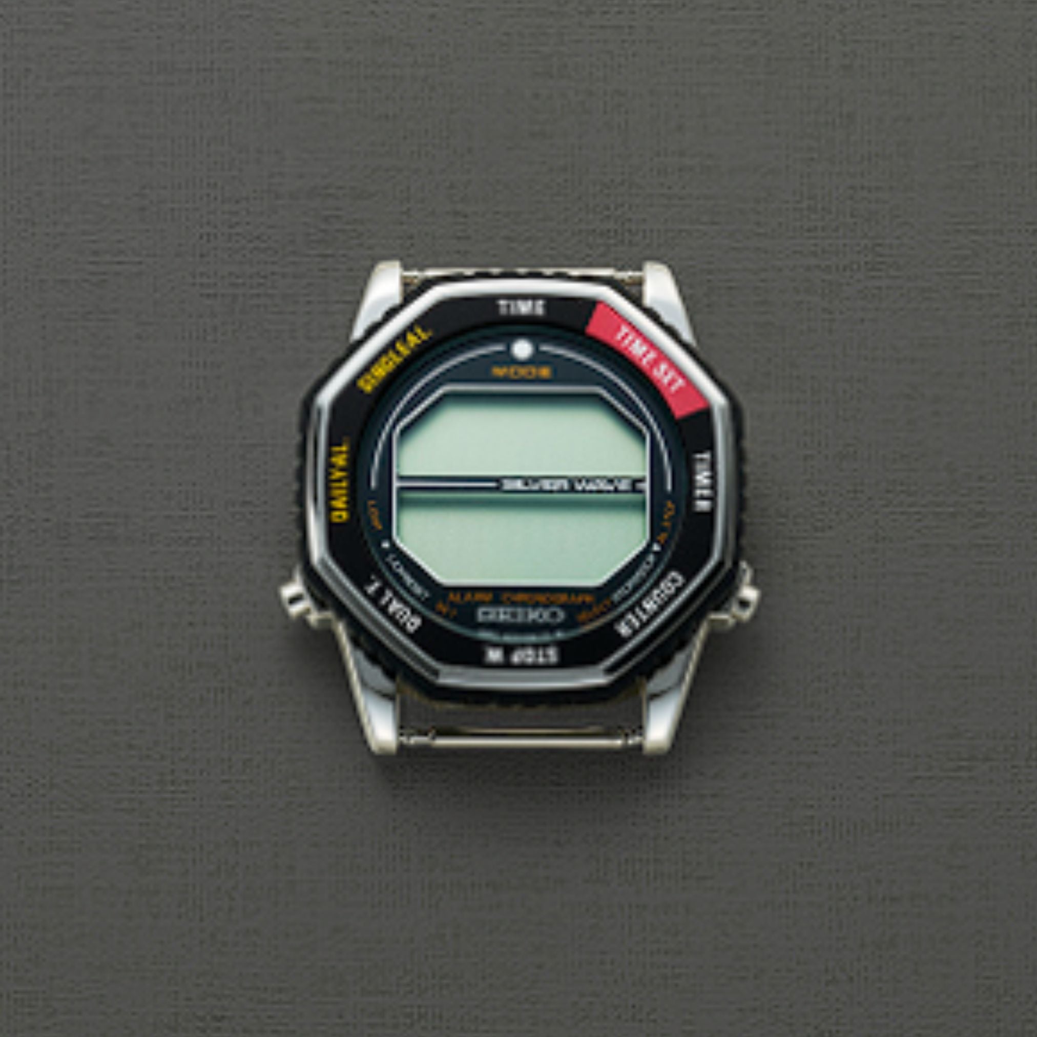 The Seiko Watches 5 Rotocall SMGG17 by Seiko Watches is a digital quartz watch with a silver case, octagonal black bezel, and a textured gray background. The bezel has yellow, white, and red mode labels but does not display the time.