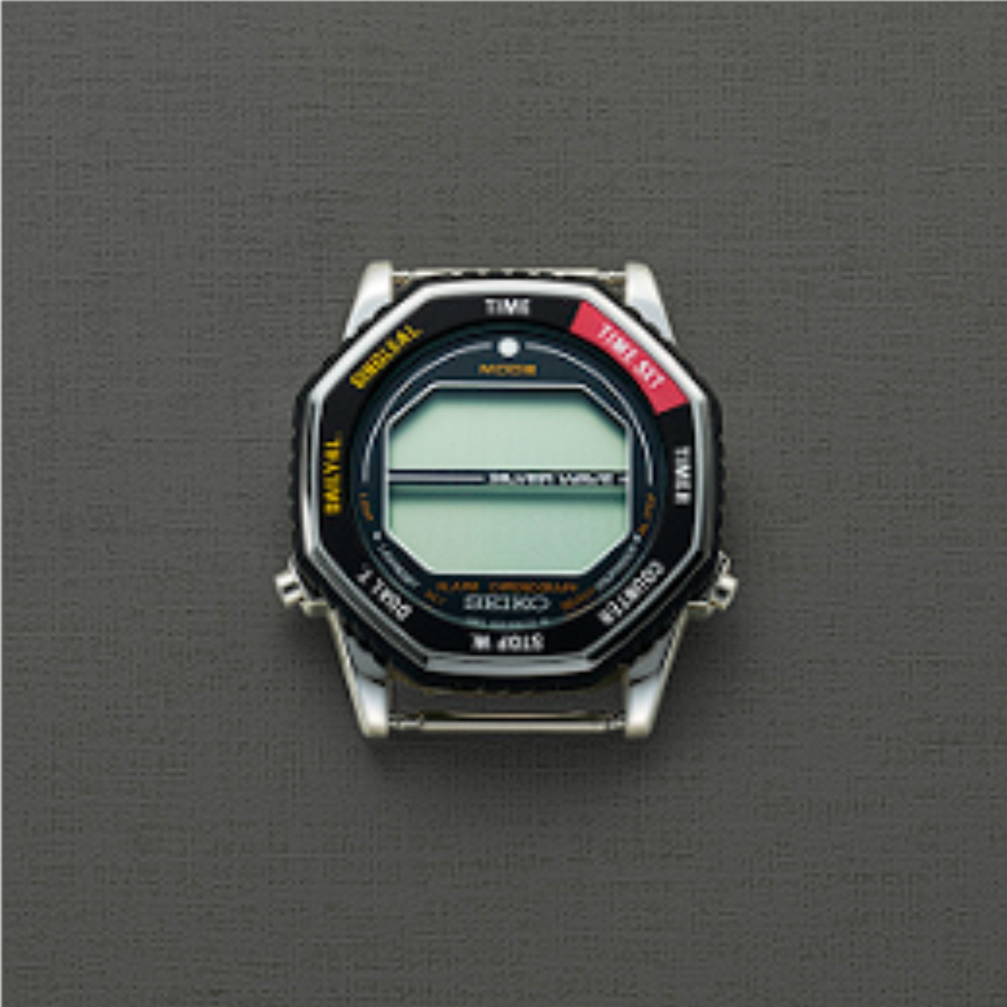 A Seiko Watches 5 Rotocall SMGG19 digital watch with a hexagonal face rests on a textured gray background, its blank screen and labeled buttons reminiscent of the classic NASA astronaut watch style.