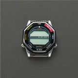 A Seiko Watches 5 Rotocall SMGG19 digital watch with a hexagonal face rests on a textured gray background, its blank screen and labeled buttons reminiscent of the classic NASA astronaut watch style.