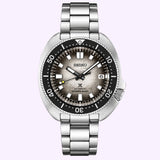 Seiko Luxe Watches PROSPEX BUILT FOR THE ICE DIVER U.S. SPECIAL EDITION SPB261, an automatic dive watch with a stainless steel band, black and silver bezel, gray textured dial, and a date window at 3 o’clock. Set against a light purple backdrop, this Ice Diver–inspired timepiece from Seiko Luxe Watches makes a bold statement.