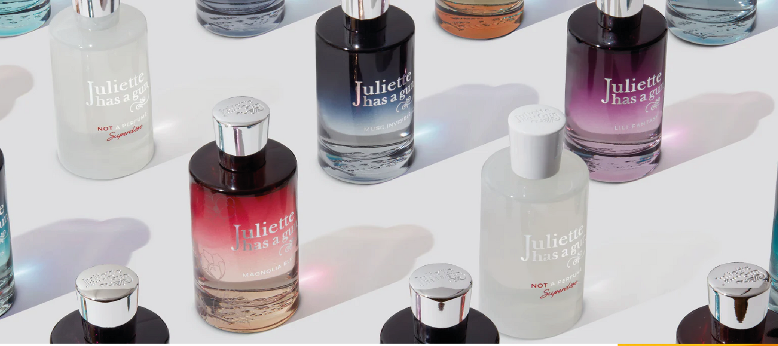 Several bottles of Juliette Has a Gun perfume are arranged on a white surface, each bottle with different colors and gradients, some with white, black, or red designs, and silver or white caps.