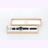 A Seiko Luxe Watches Presage Green Enamel Limited Edition SPB111 men’s watch, featuring a striking green enamel face and brown leather strap, is displayed elegantly in an open wooden box.