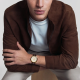 A man wearing a Tissot T1294103626100 CLASSIC DREAM Men Watch with a gold-tone case, cream dial, and brown leather strap on his wrist.