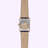 A close-up of the Frederique Constant Classics Carrée FC-311S4C4-BL wristwatch highlights its exposed mechanical movement and engraved beige leather straps, set against a light purple background.