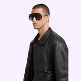 Wearing Carrera Sunglasses FLAGLAB 17 2M2 (UPC: 197737075071) and a black leather jacket, a person stands against a light purple background, looking to the side with a neutral expression.