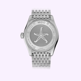 The back of the Mido Watch OCEAN STAR GMT M0268291804100 by Mido Watches, with a metal bracelet and starfish engraving, highlights Swiss craftsmanship against a light purple background.