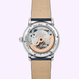 A close-up of the Frederique Constant Manufacture Classic Worldtimer FC-718NWM4H6 reveals its exposed Swiss automatic movement, rose gold rotor, silver case, beige leather strap, and engraved text surrounding the transparent case back.