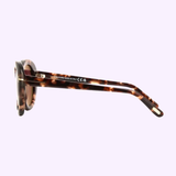 Side view of Tom Ford FT1009 55 55Y Lily-02 Woman Acetate Sunglasses by Tom Ford Sunglasses, featuring thick round tortoiseshell-patterned frames and brown arms, set against a light purple background.