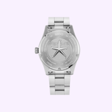 The Mido Watches Ocean Star 39 M0269071104101 is shown from the back, displaying its engraved case back with a central starfish emblem and metal link bracelet, all set against a light purple background.