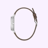 Side view of the Bulova Watches 96A314 Ennis House men’s watch by Bulova Watches, featuring a silver round case and brown leather strap with metal buckle and two loops, set against a light lavender background.