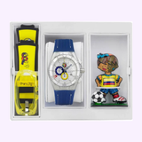 ThechnoMarine 114023 Cruise Tribute Columbia Edition By Britto Unisex watch set by Thechnomarine Watches includes a blue and silver watch with colorful accents, two extra straps, and a cartoon soccer figurine, all in a white gift box.