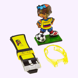 A soccer player figurine, yellow cartoon wristband with number 21, and a yellow accessory capture the sporty vibe of the Thechnomarine 114023 Cruise Tribute Columbia Edition By Britto Unisex Watch by Thechnomarine Watches.