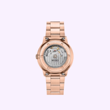 The Mido Watch Commander Datoday M0214303309100 by Mido Watches features a rose gold automatic design with a visible mechanical movement and transparent sapphire case back, displayed on a light purple background.