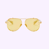 A pair of Balmain BPS-125C-62 Capitane Unisex Sunglasses by Balmain Sunglasses, featuring thin gold aviator frames and yellow-tinted lenses, displayed against a pale lavender background.