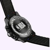 A close-up of the Tissot Watches Supersport NBA Special Edition T1256173706700 shows the NBA logo engraved on the case. The black quartz chronograph, with a black strap and side buttons, stands out against a light purple background.