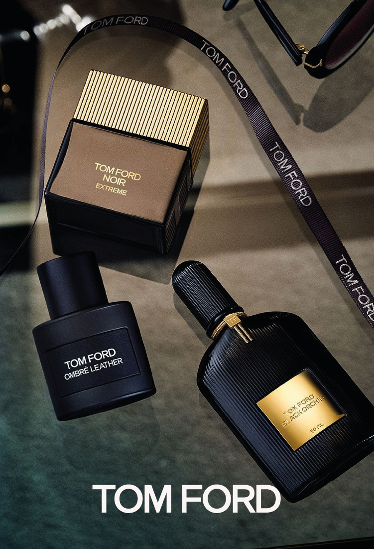 Three Tom Ford perfume bottles—Noir Extreme, Ombre Leather, and Black Orchid—are arranged on a glass surface with a Tom Ford-branded ribbon and sunglasses. The Tom Ford logo appears at the bottom.