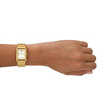 A left hand displays the Tory Burch Watches THE ELEANOR TBW1060 women’s watch—an elegant gold-tone wristwatch with a rectangular face and Roman numerals—set against a white background.