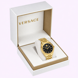 A Versace VE6A00623 V-Code men’s watch from Versace Watches, featuring a gold-tone case and a black dial, is elegantly presented on a cushioned holder in an open white and gold Versace box against a light background—a stunning Swiss-made luxury timepiece.