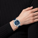Wearing a ribbed black long-sleeve top, a person displays the Versace Watches VEVCA0124 V-Chrono Square Leather Watch (UPC 198218260801) on their wrist—a luxury chronograph timepiece with a blue face and blue strap, featuring precise Swiss quartz movement—as their hand rests on their opposite arm.