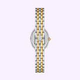The Tory Burch Watches THE OVAL TBW6033 women’s watch by Tory Burch Watches is displayed from the back. It features a silver and gold two-tone metal band, a round case showcasing the logo at its center, and a visible crown on the right side. The background is light purple.