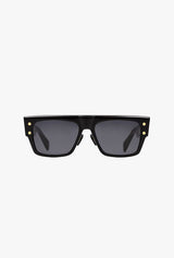 Balmain B-I BPS-100A 56 Unisex Sunglasses: black rectangular frames with thick borders and dark lenses, detailed with gold rivets at the corners—all set against a plain white background, showcasing Balmain Sunglasses style.