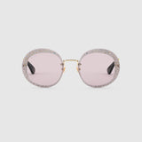 Gucci GG0899S 001 61 Women Sunglasses by Gucci feature oversized gold frames, thick rims adorned with sparkling crystals, and pale pink lenses, showcased on a plain light gray background.