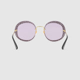 Gucci GG0899S 001 61 women sunglasses with round light purple lenses, gold bridge and accents, black arms, and a patterned frame, shown on a plain light gray background.