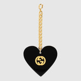 A gold chain keychain displays a black heart-shaped pendant with a gold Gucci logo, echoing the iconic design of the Gucci GG0977S 001 57 Women Sunglasses by Gucci Sunglasses, shown on a plain light gray background.