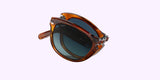 A pair of Persol PO0714SM 96/S3 54 Unisex Sunglasses by Persol Sunglasses is folded neatly against a light purple background.
