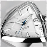 Close-up of the Hamilton H24505311 Ventura Elvis80 Auto by Hamilton Watches—a unisex watch with a distinctive triangular white dial, silver markers and hands, blue seconds hand, date at 3 o’clock, and automatic movement on a white silicone strap.
