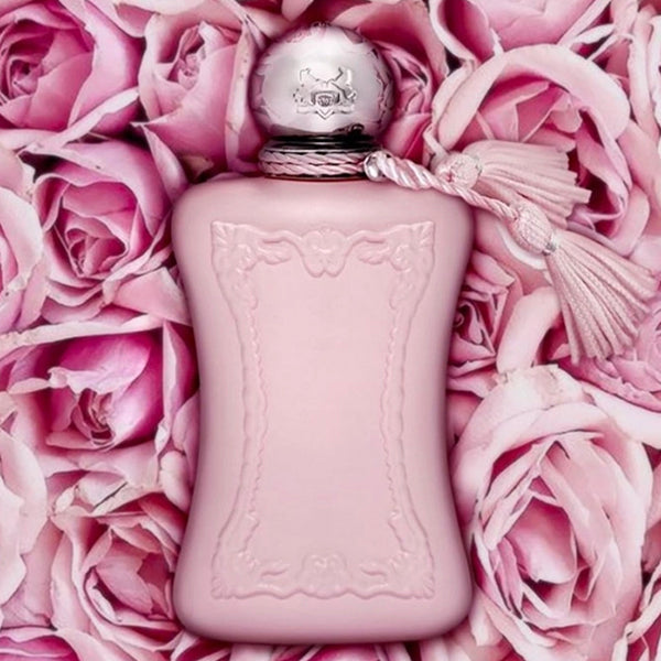 A matte pink Parfums de Marly Delina 2.5 oz EDP for Women bottle, adorned with embossed details and a tasseled cap, rests among rose petals, reflecting the floral elegance of Parfums De Marly Perfumes.