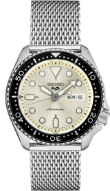 The Seiko SRPE75 5 Series by Seiko Watches is a men's watch featuring a silver stainless steel mesh strap, cream dial, black bezel with white markers, luminous hands and indices, and a day-date window at 3 o’clock.