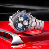 A Tissot T1316171104200 PRS 516 Chronograph Men’s Watch by Tissot Watches, featuring a blue and white dial, sits on a shiny red car near a metallic intake vent.